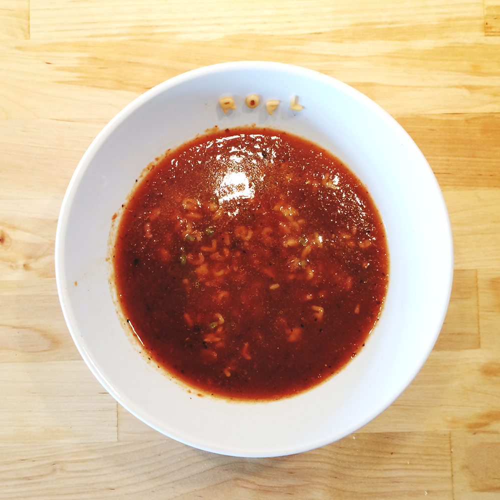 A photo of a white bowl of tomato soup with alphabet pasta. The letters ROFL are stuck on the inside of the bowl above the soup line.