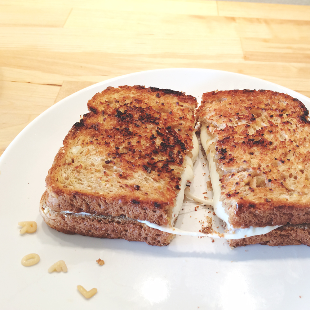 A grilled cheese sandwich on a plate. The sandwich is cut in half and the cheese is being “pulled.” The ROFL letters are now on the plate.