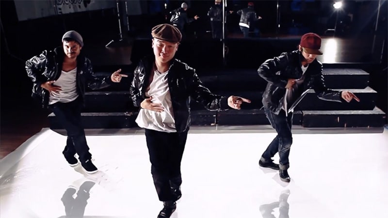 A still from a Youtube dance video by Mike Song. Mike Song, Mikey Andaya, and Lawrence Kao are mid-dance. They're all wearing shiny leather jackets and different hats.