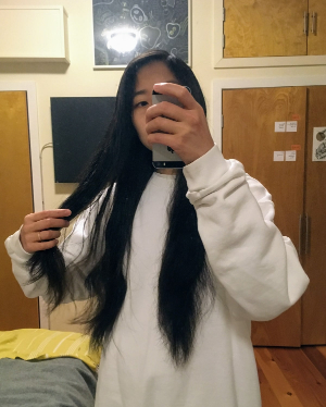 Mirror selfie. I’m wearing a white sweatshirt. My hair is super long, and it’s coming down the front of my sweatshirt, maybe down to where the navel would be. I’m holding my phone with one hand, and holding up some of my hair with the other.